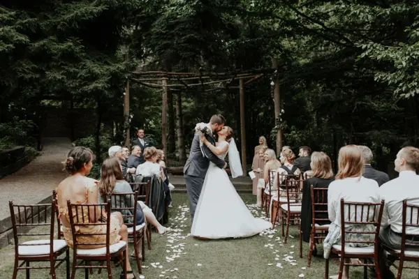 Bride and groom kissing at outdoor Pacific Northwest wedding ceremony in forest setting. Lovely Events.